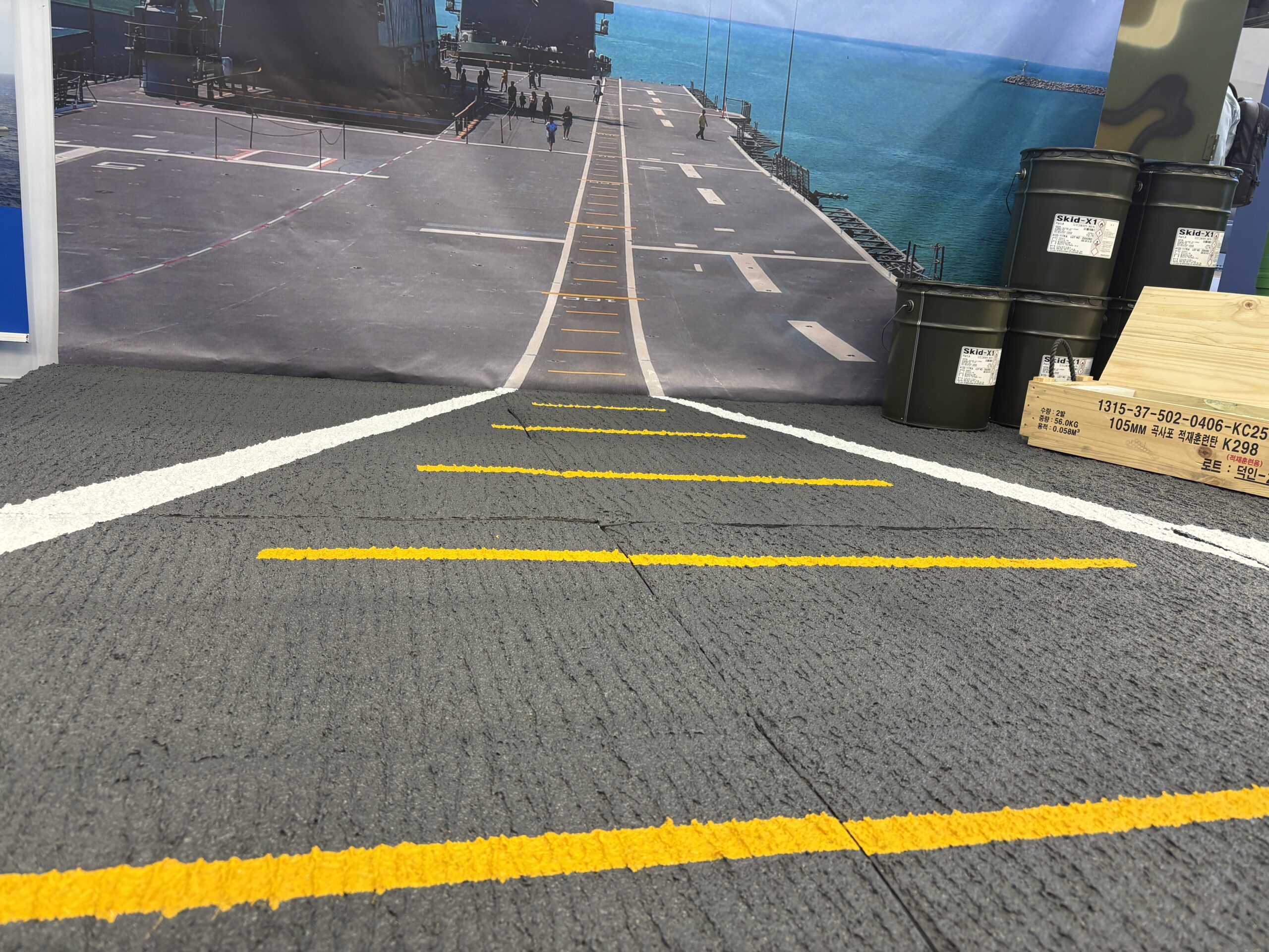 MADEX 2025의 주영산업(주) MIL-X COATING 부스 전시물 사진. 군함 데크 활주로를 배경으로 미끄럼 방지 도료인 Skid-X 제품 도장이 되어 있어 시선을 끈다.